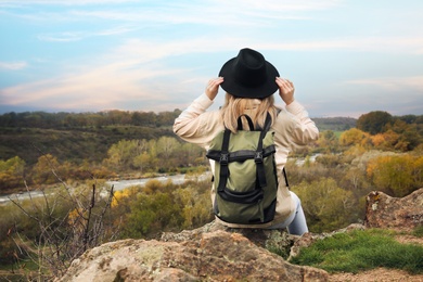 Photo of Woman with travel backpack sitting on steep cliff near mountain river, back view