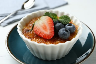 Delicious creme brulee with berries and mint in bowl on white table, closeup