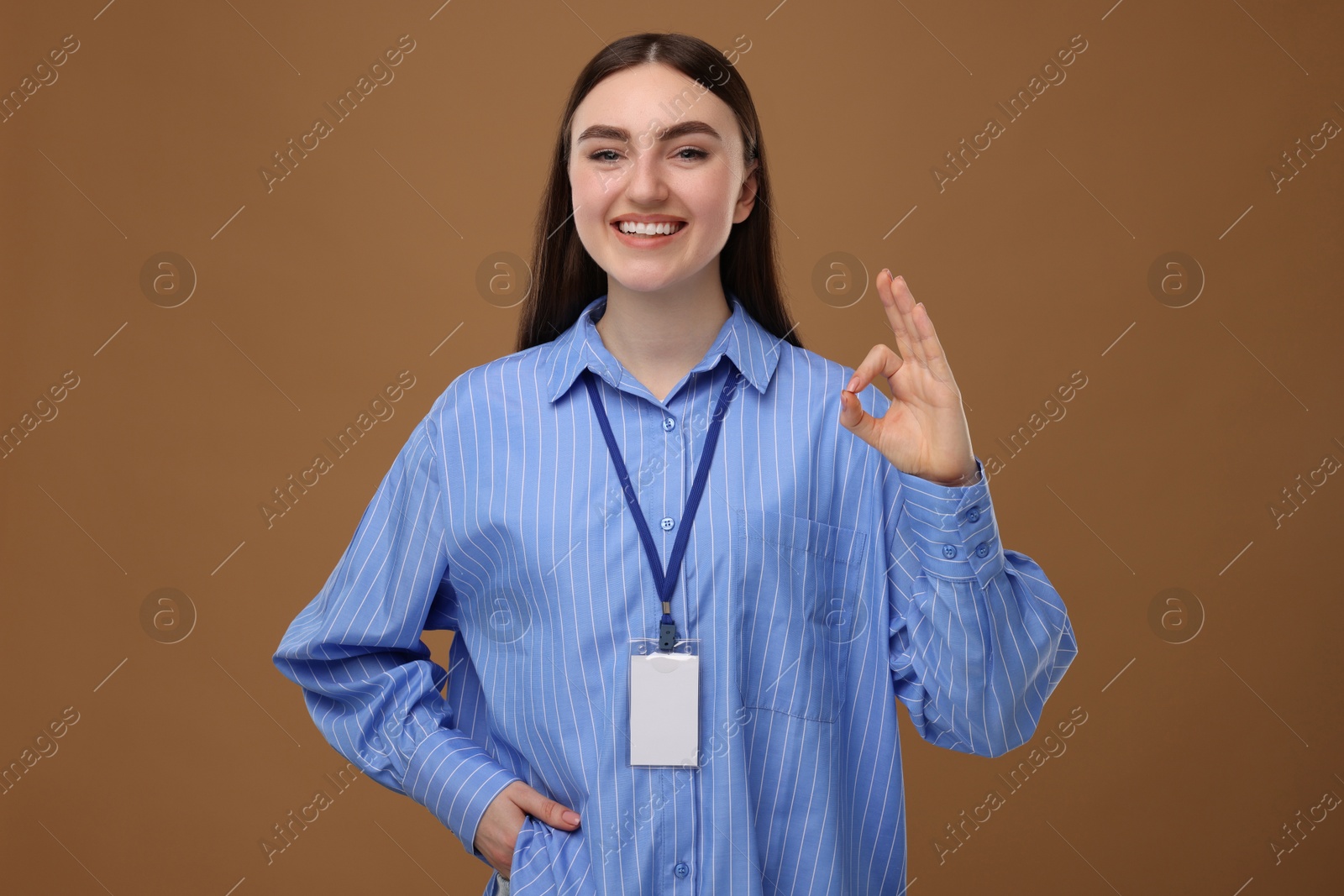 Photo of Happy woman with blank badge showing ok gesture on brown background
