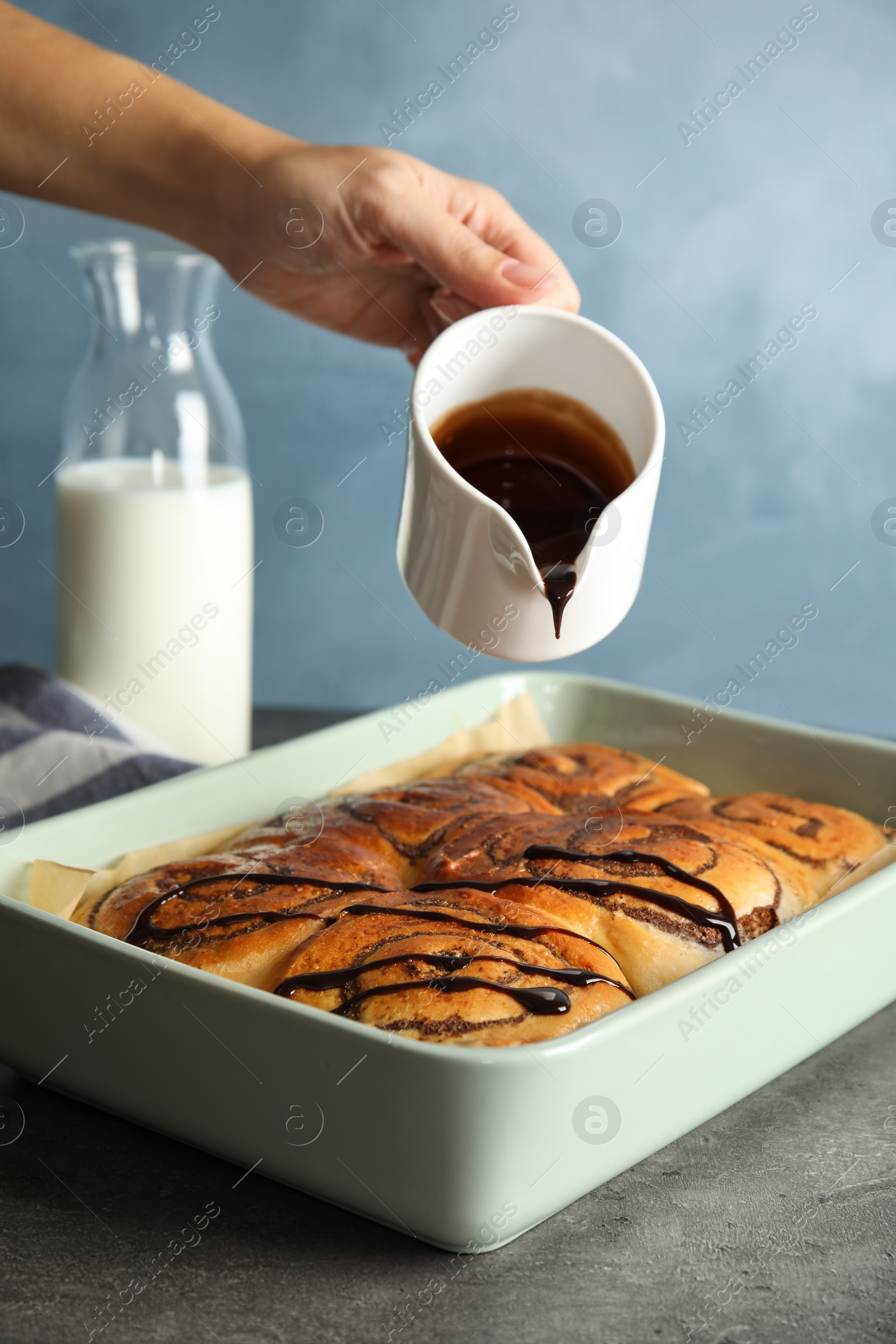 Photo of Woman pouring chocolate syrup onto freshly baked cinnamon rolls on table, closeup