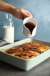 Woman pouring chocolate syrup onto freshly baked cinnamon rolls on table, closeup