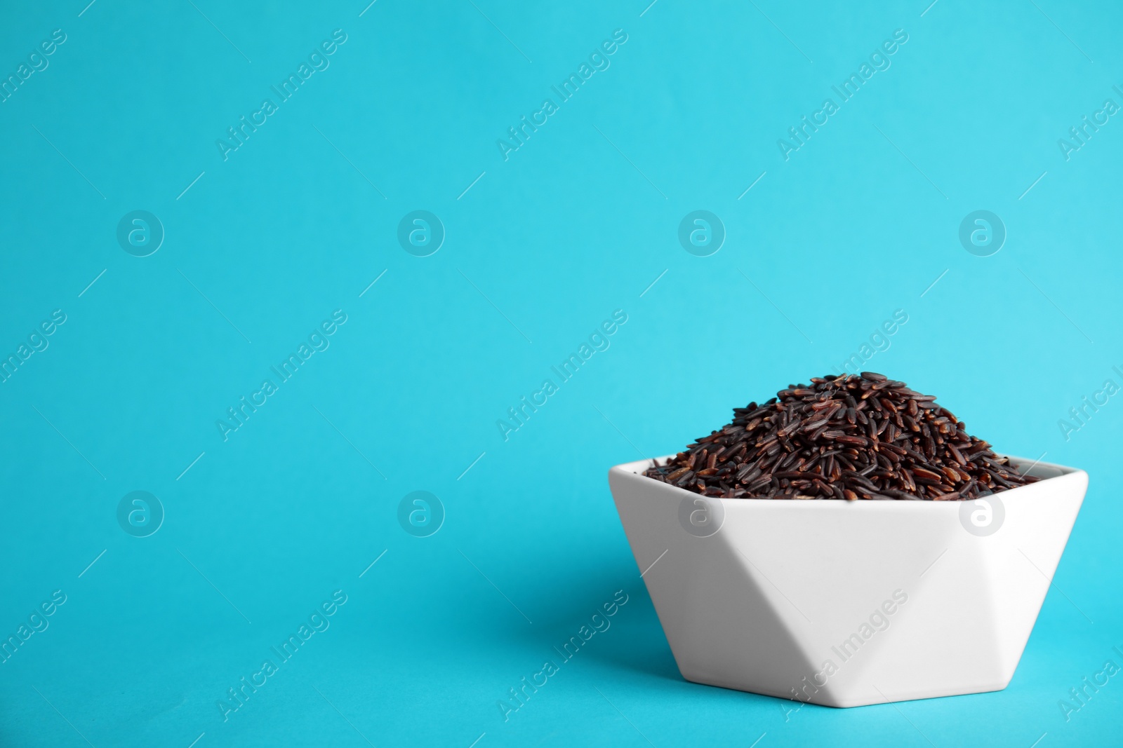 Photo of Bowl with uncooked black rice on color background. Space for text