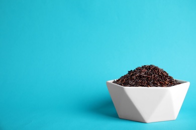 Bowl with uncooked black rice on color background. Space for text