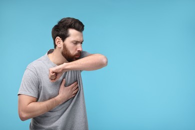 Sick man coughing into his elbow on light blue background, space for text. Cold symptoms
