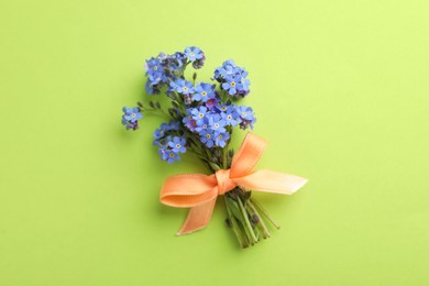 Beautiful blue forget-me-not flowers tied with ribbon on light green background, top view