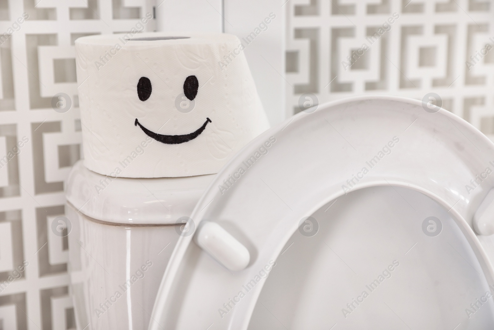 Photo of Roll of paper with funny face on toilet tank in bathroom, closeup