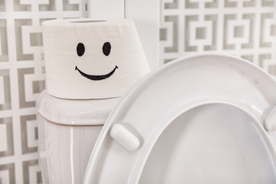 Photo of Roll of paper with funny face on toilet tank in bathroom, closeup