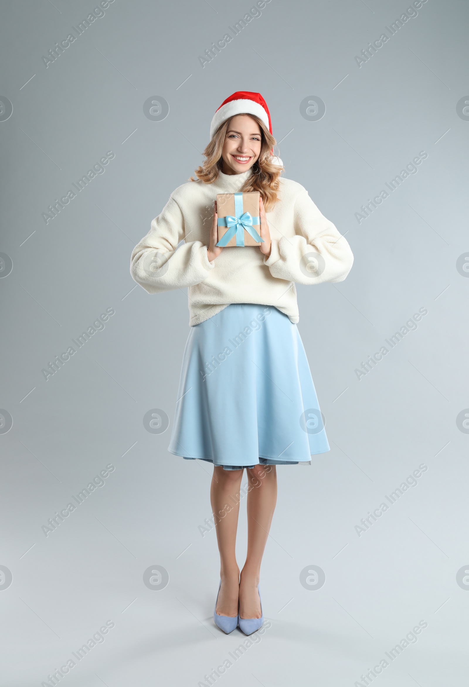 Photo of Beautiful young woman in Santa hat with Christmas present on light grey background