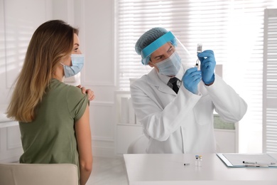 Photo of Doctor filling syringe with vaccine against Covid-19 while patient waiting for injection in clinic