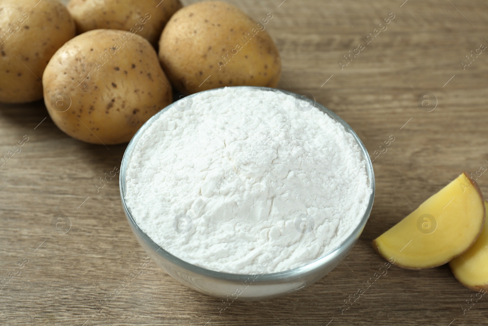 Photo of Glass bowl with starch and fresh potatoes on wooden table