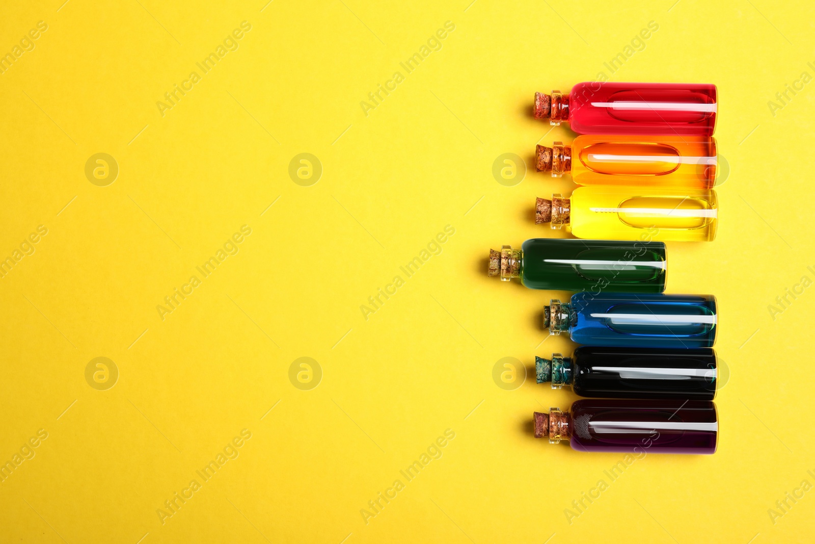 Photo of Bottles with different food coloring on yellow background, flat lay. Space for text