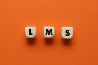 Learning management system. Wooden cubes with abbreviation LMS on orange background, top view