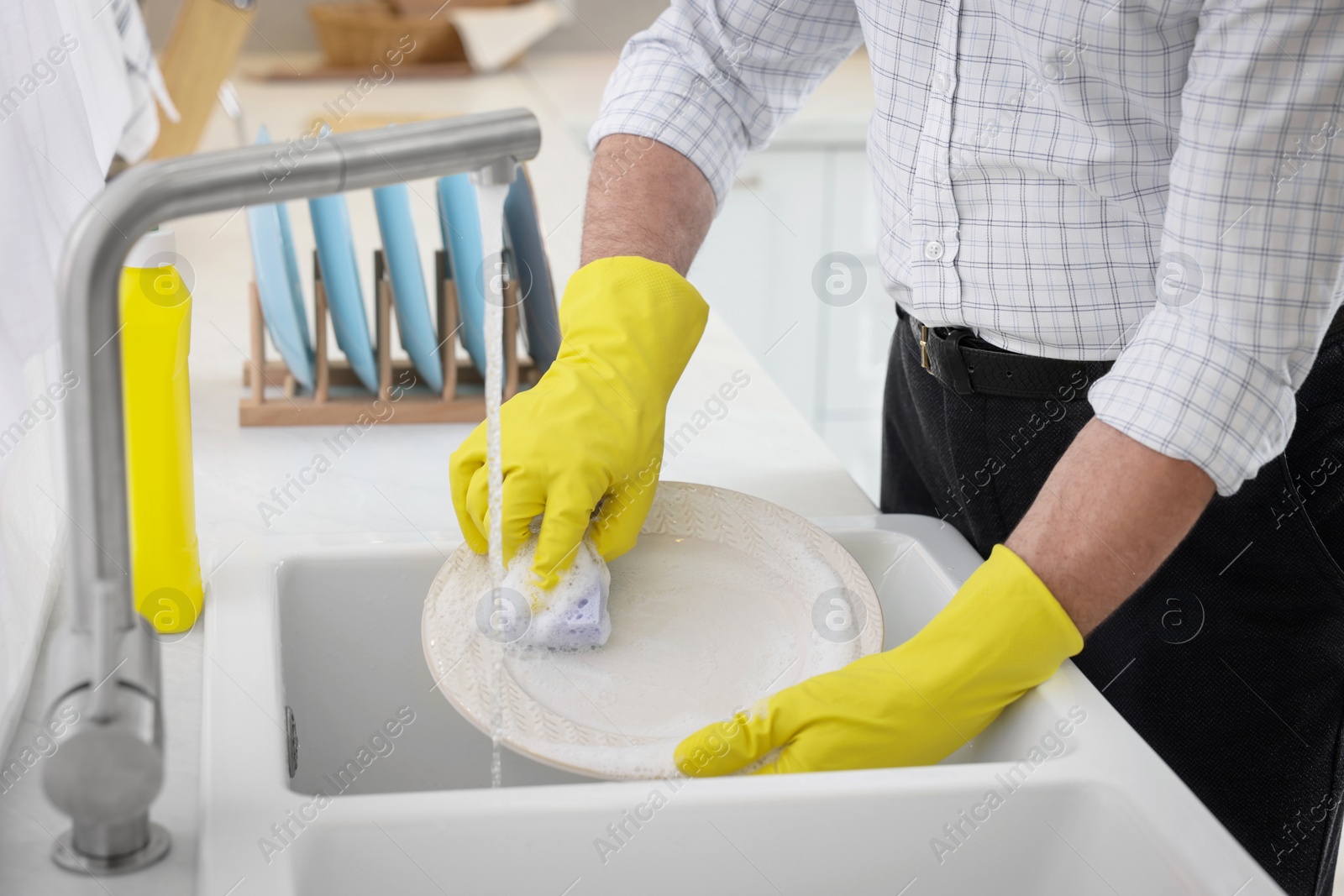 Photo of Man in protective gloves washing plate above sink in kitchen, closeup