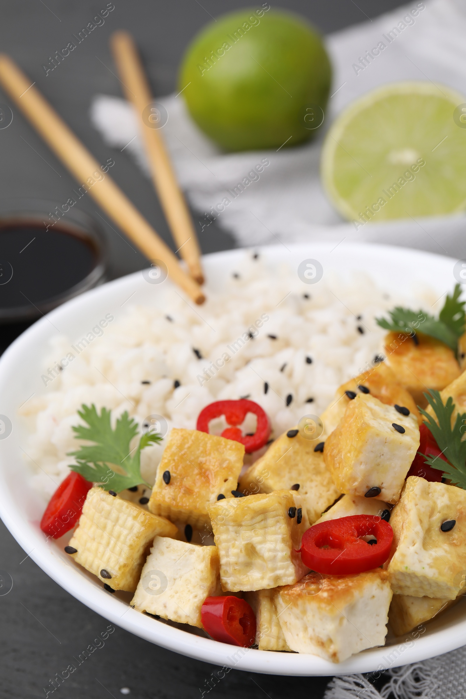 Photo of Bowl of rice with fried tofu, chili pepper and parsley on grey wooden table, closeup