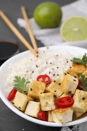 Photo of Bowl of rice with fried tofu, chili pepper and parsley on grey wooden table, closeup