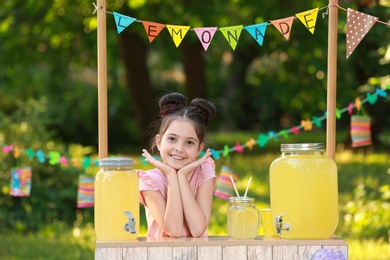 Photo of Cute little girl at lemonade stand in park. Summer refreshing natural drink