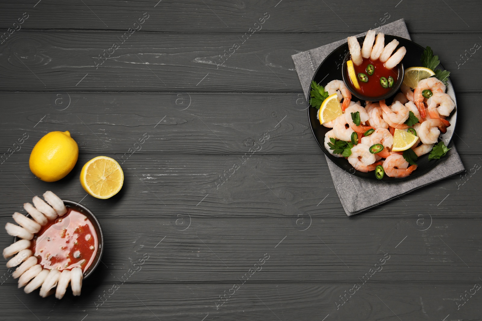 Photo of Tasty boiled shrimps with cocktail sauce, chili, parsley and lemon on grey wooden table, flat lay. Space for text