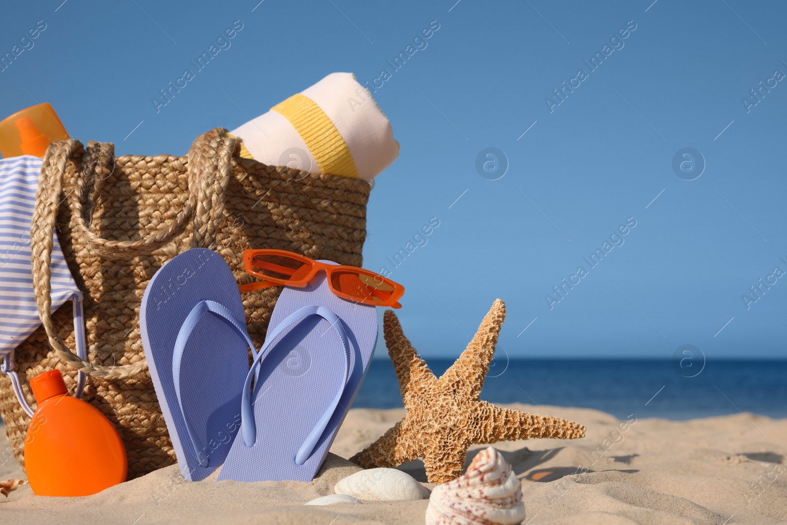 Photo of Bag and beach accessories on sand near sea. Space for text