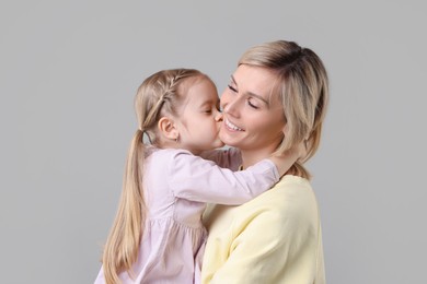 Daughter kissing her happy mother on grey background