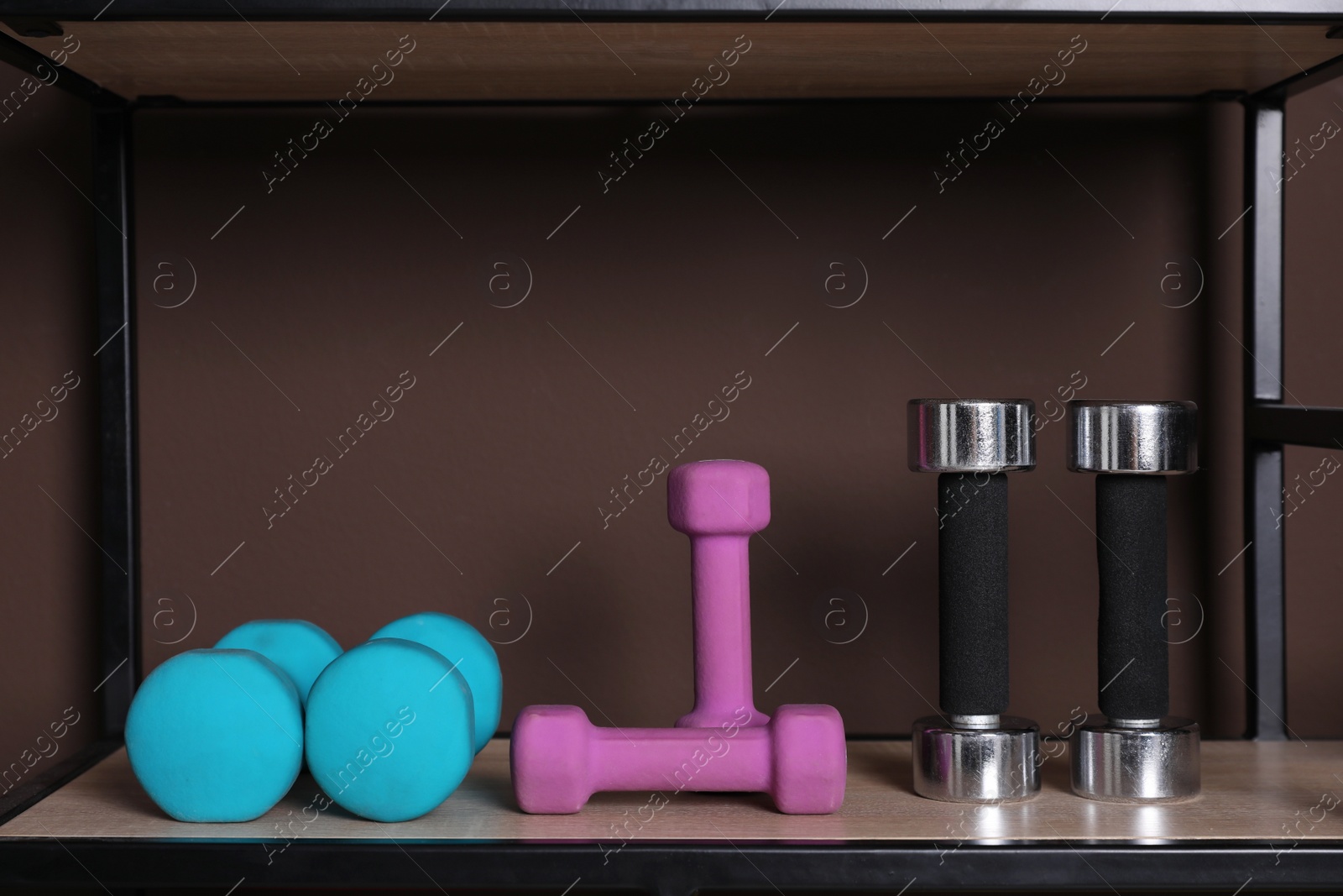 Photo of Different dumbbells on shelf near brown wall. Sports equipment
