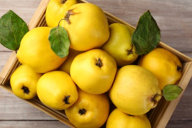 Photo of Tasty ripe quince fruits in crate on wooden table, top view