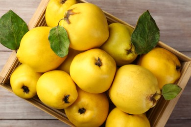 Tasty ripe quince fruits in crate on wooden table, top view