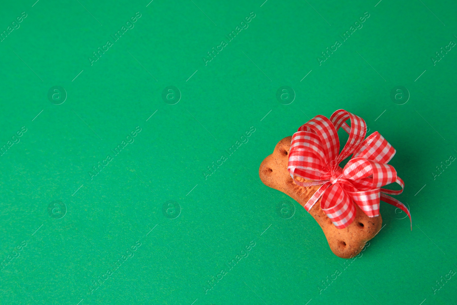 Photo of Bone shaped dog cookie with red bow on green background, top view. Space for text
