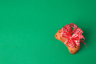 Bone shaped dog cookie with red bow on green background, top view. Space for text