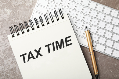 Image of Notebook with words TAX TIME and keyboard on grey marble table, flat lay