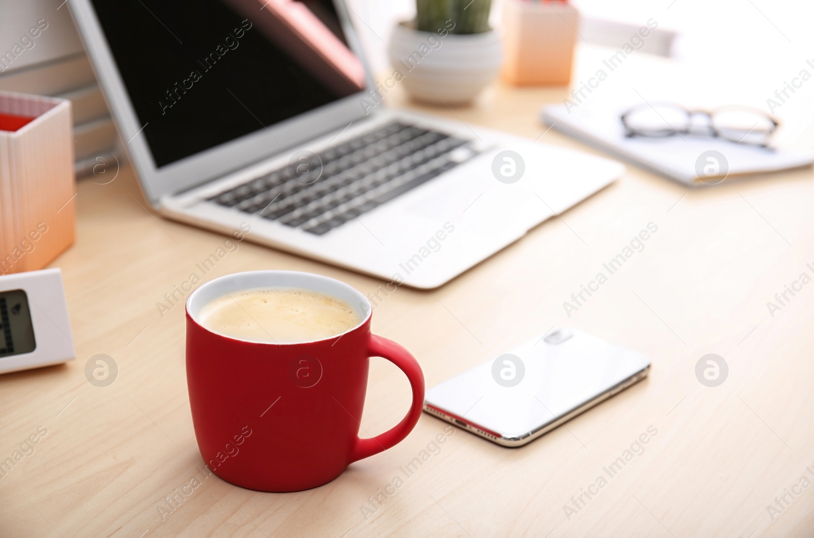 Photo of Red cup with coffee and phone near laptop on office table. Break time