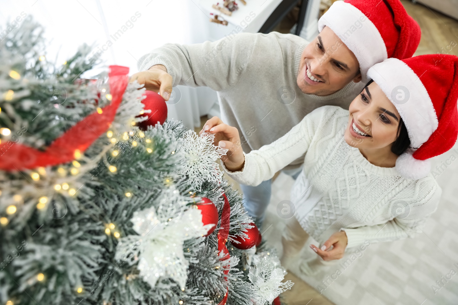 Photo of Happy couple decorating Christmas tree at home, above view