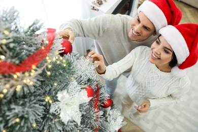 Photo of Happy couple decorating Christmas tree at home, above view