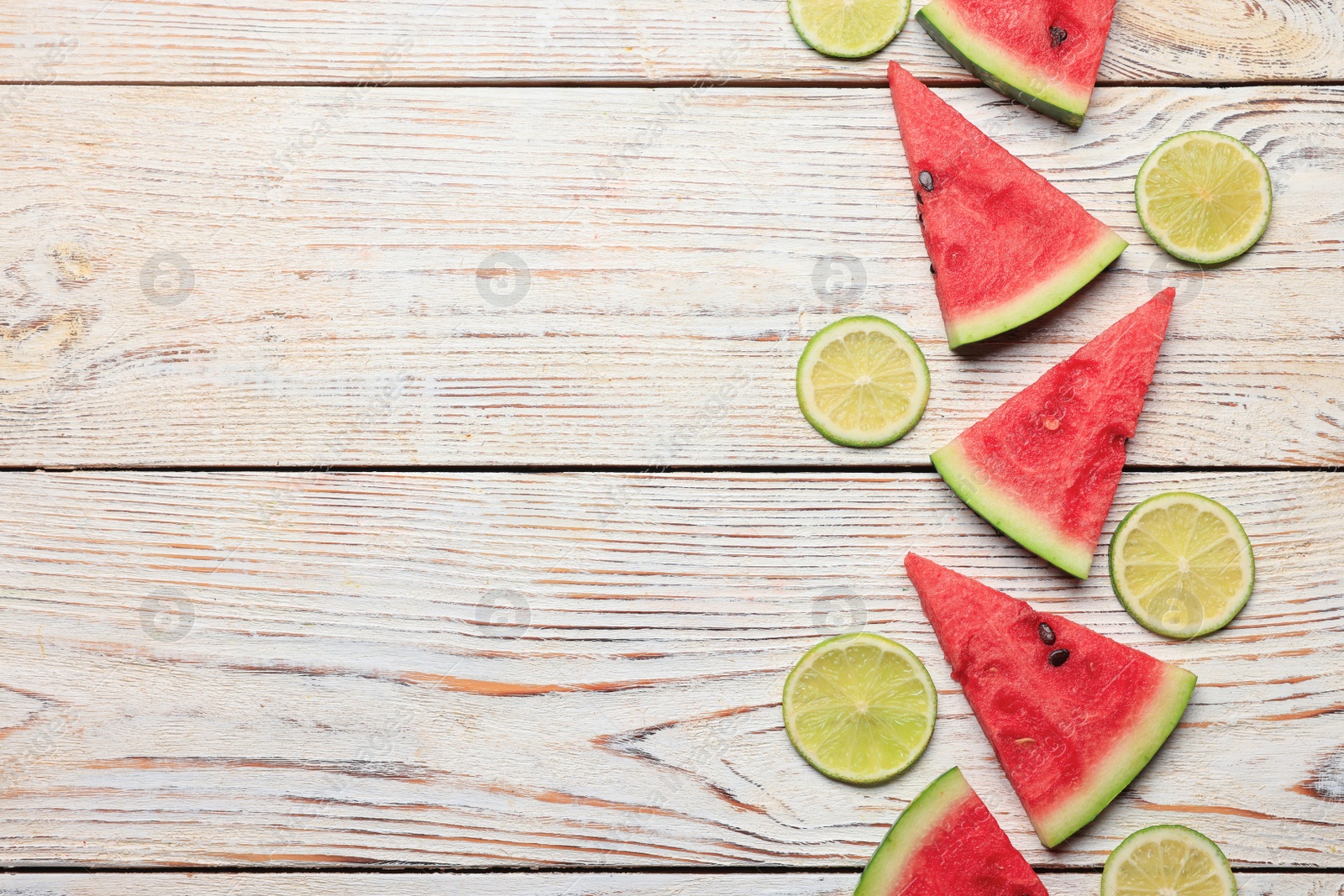 Photo of Tasty sliced watermelon and limes on white wooden table, flat lay. Space for text