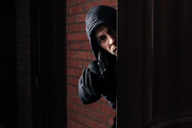 Man with gun spying behind open door indoors. Criminal offence