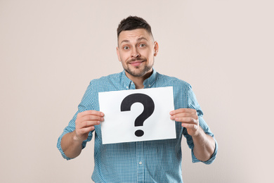 Emotional man holding paper with question mark on grey background