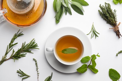 Aromatic herbal tea with thyme, rosemary, mint and sage on white table, flat lay