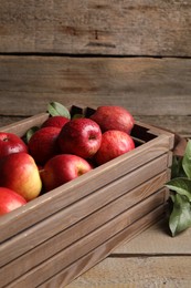 Ripe red apples with water drops in crate and green leaves on wooden table