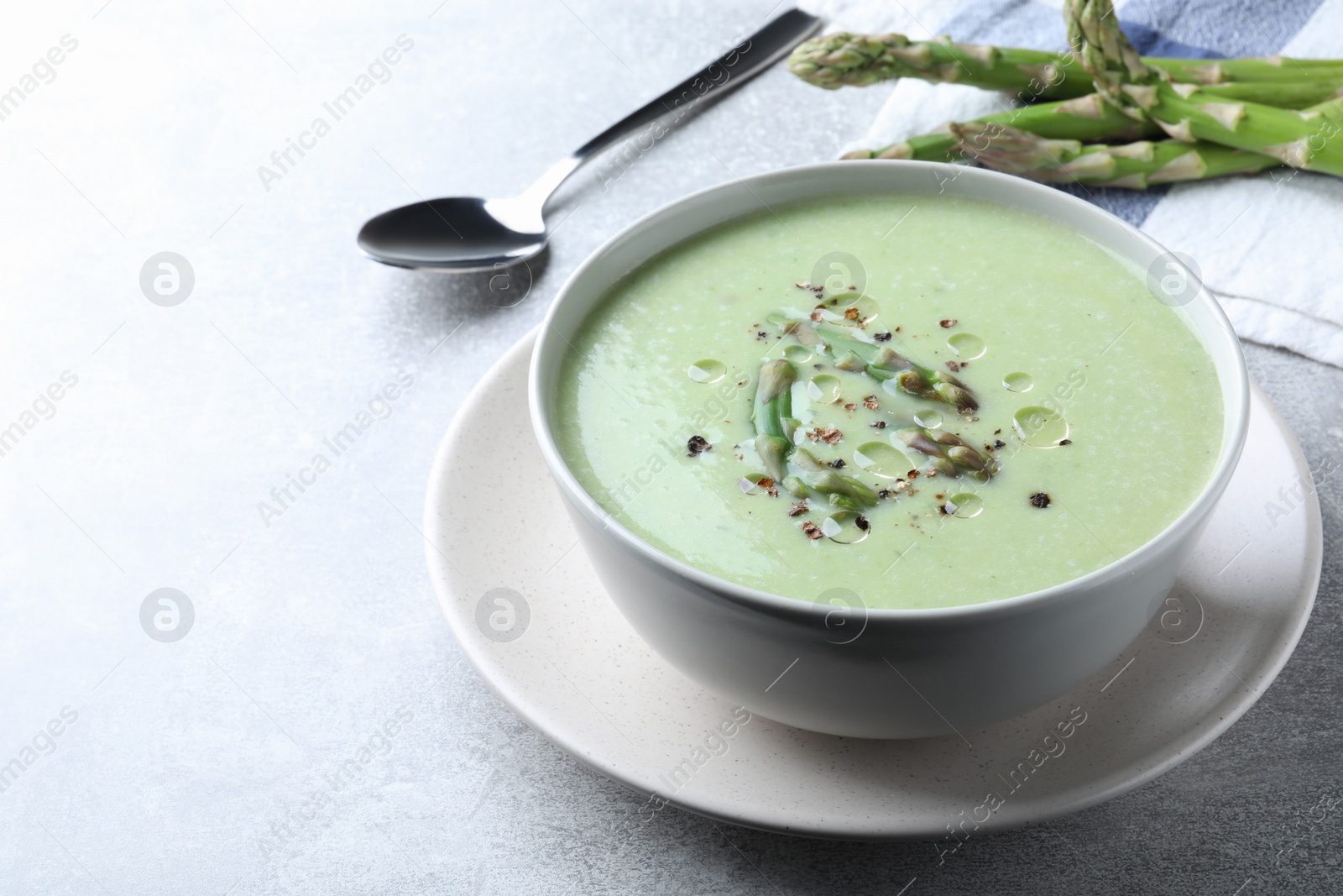 Photo of Delicious asparagus soup served on light grey table, space for text