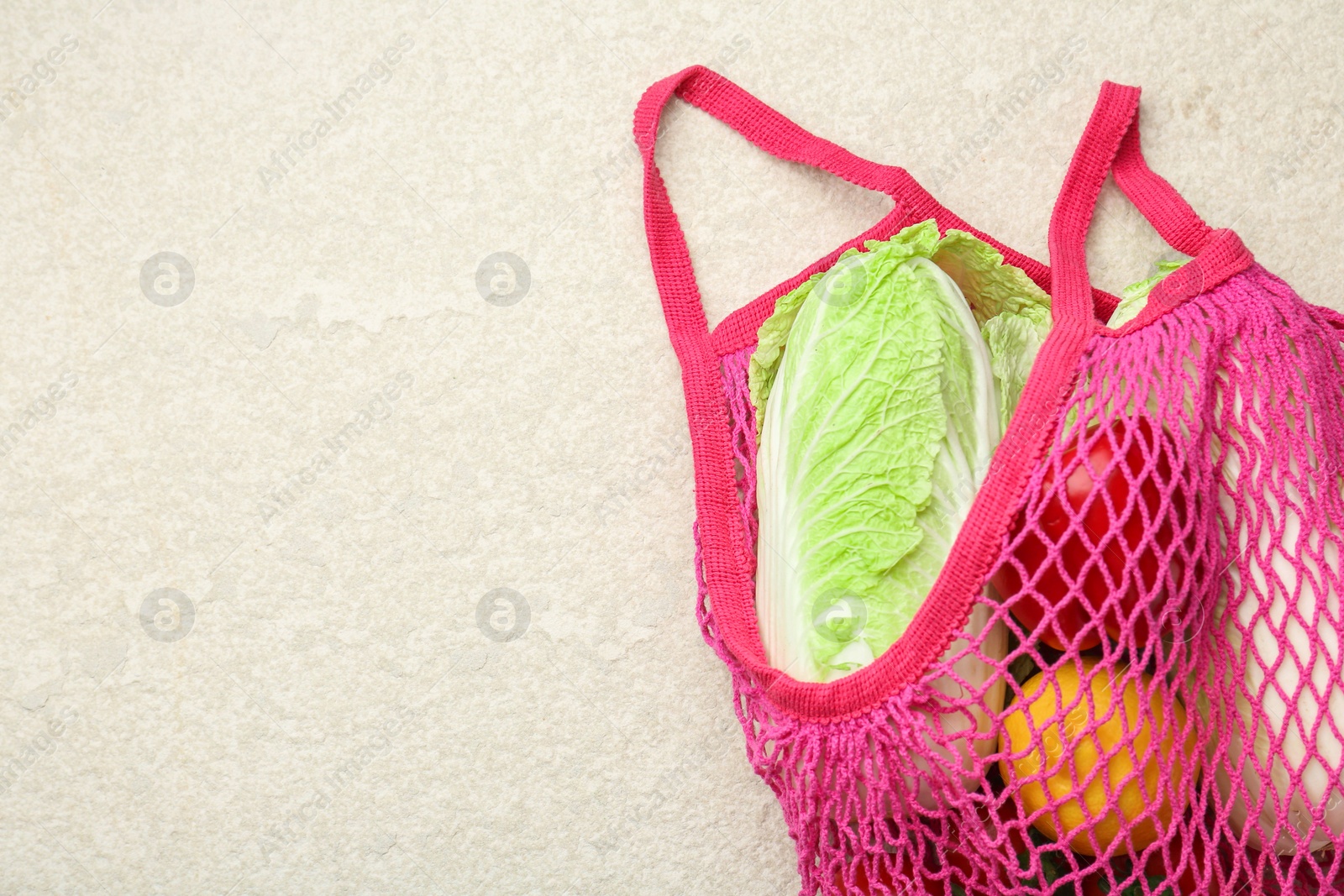 Photo of Fresh Chinese cabbage and other products in string bag on light textured table, top view. Space for text