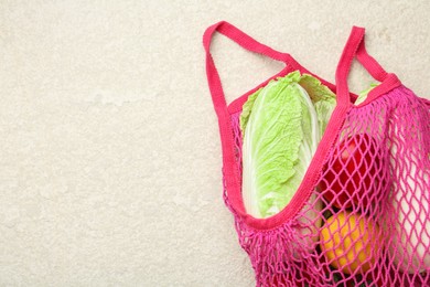 Fresh Chinese cabbage and other products in string bag on light textured table, top view. Space for text