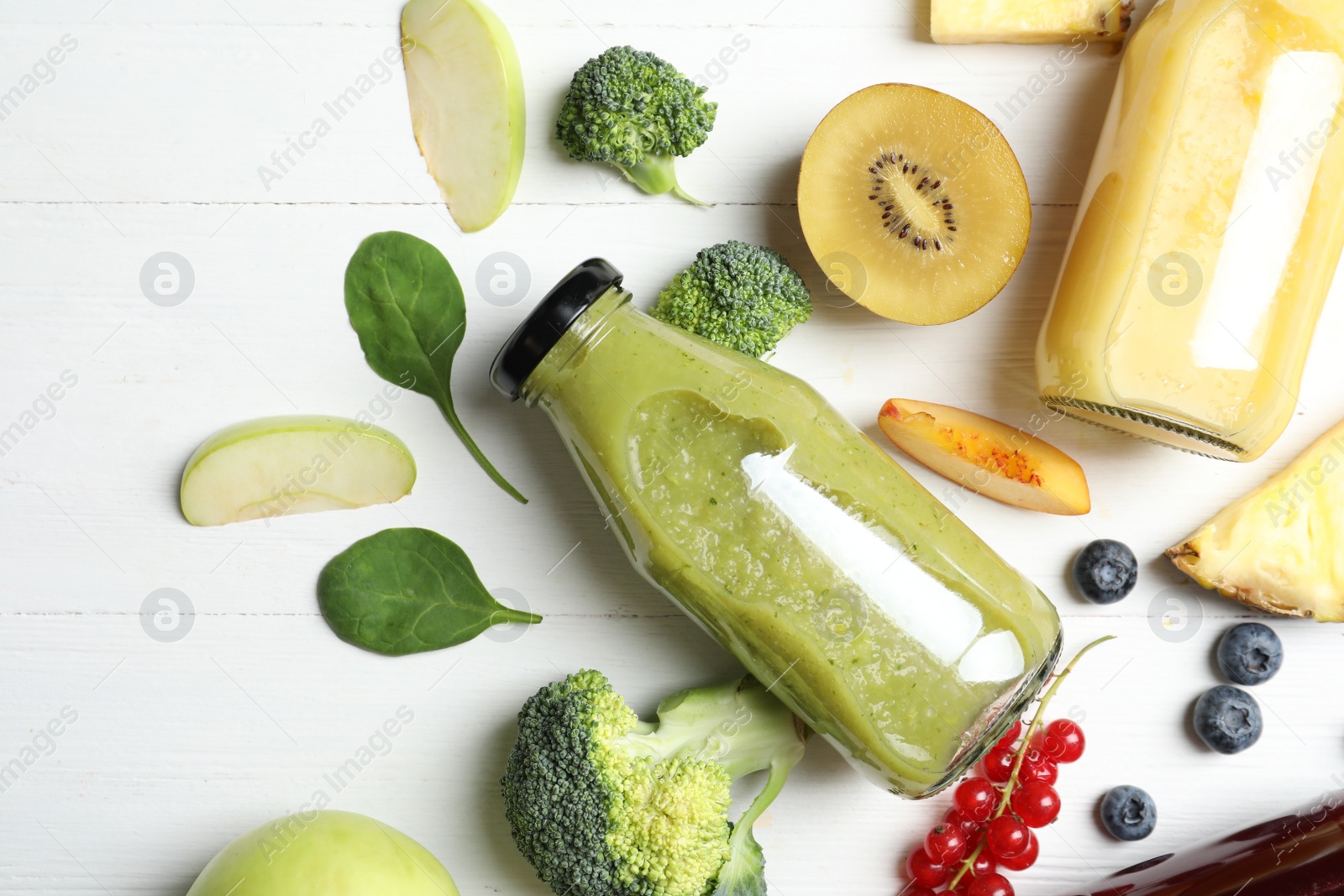 Photo of Bottles of delicious juices and fresh fruits on white wooden table, flat lay