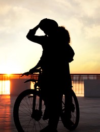 Image of Silhouette of lovely couple with bicycle on city waterfront at sunset