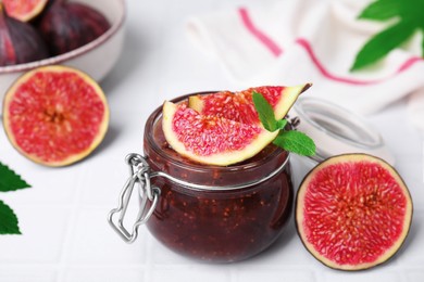 Photo of Glass jar of tasty sweet fig jam and fruits on white tiled table