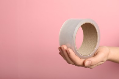 Photo of Woman holding transparent adhesive tape on pink background, closeup. Space for text