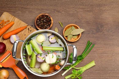 Photo of Pot and different ingredients for cooking tasty bouillon on wooden table, flat lay. Space for text