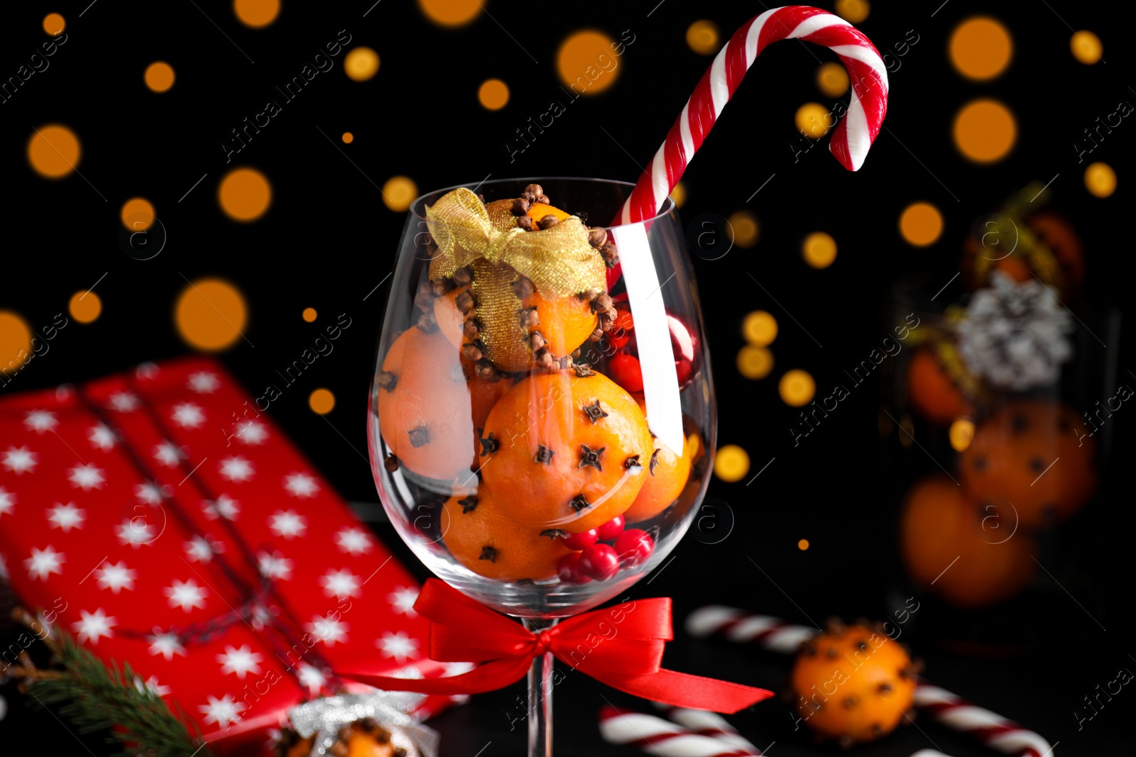 Photo of Christmas composition with tangerine pomander balls in wineglass against blurred lights