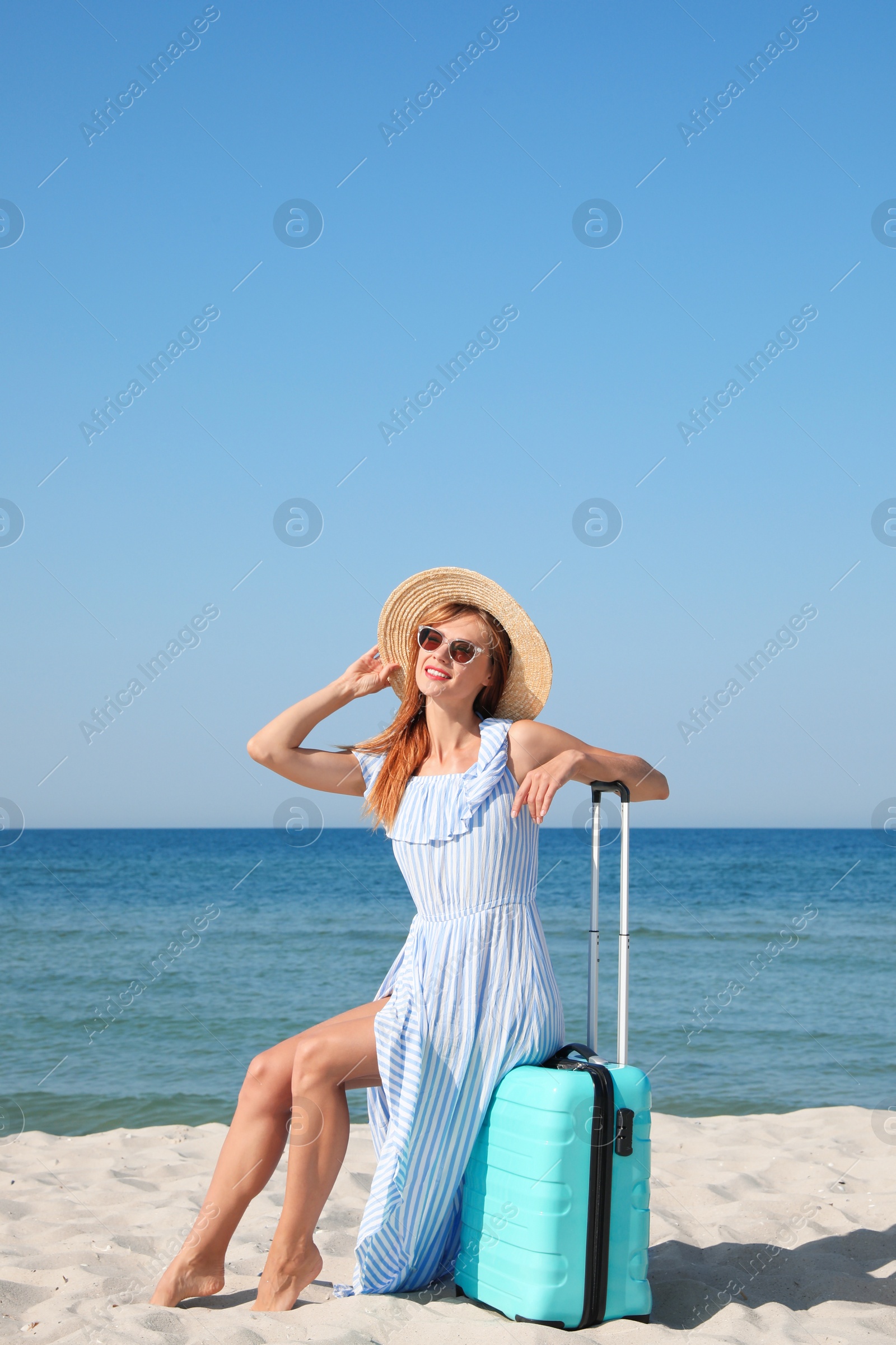 Photo of Beautiful woman with suitcase on sandy beach near sea