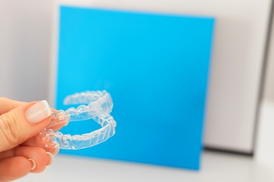 Photo of Woman with transparent dental aligners on blurred background, closeup. Space for text