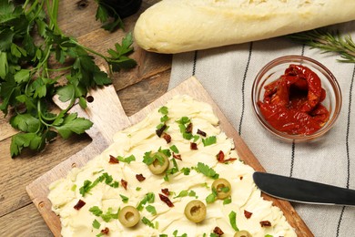 Photo of Fresh butter board with cut olives, sun-dried tomatoes, bread and knife on wooden table, flat lay