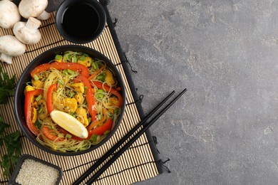 Photo of Stir-fry. Delicious cooked noodles with chicken and vegetables in bowl served on gray textured table, flat lay. Space for text